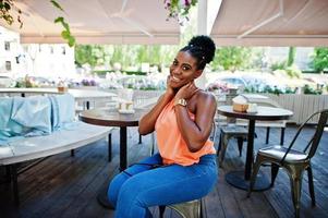 chica afroamericana sentada en la mesa de café y posada. foto