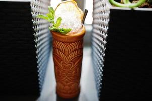 Alcoholic cocktail with mint in originally voodoo earthen glass on bar table. photo