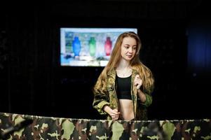 Military girl in camouflage uniform against army background on shooting range. photo