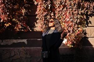 Stylish african american girl in blue coat and sunglasses posed at sunny autumn day. Africa model woman. photo