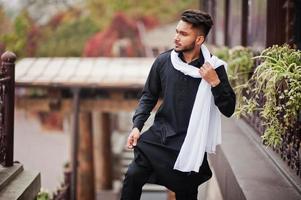 Indian stylish man in black traditional clothes with white scarf posed outdoor. photo