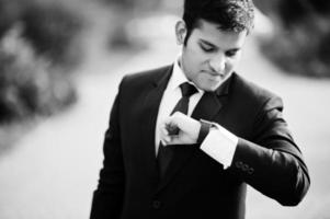 Elegant south asian indian business man in black suit looking at his smart watches on hand. photo