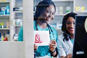 Two african american pharmacist working in drugstore at hospital pharmacy. African healthcare. Cashier holding sale. photo