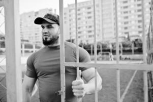 Young brutal bearded muscular man wear on red shirt, shorts and cap at stadium. photo