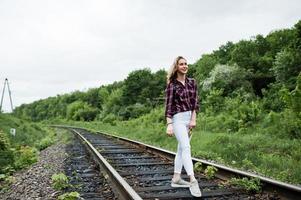 retrato de una linda chica rubia con camisa de tartán caminando por el ferrocarril con un mapa en las manos. foto