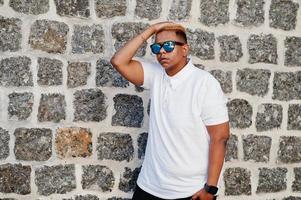 Stylish arabian muslim boy with originally hair and sunglasses posed on streets against brick wall. photo