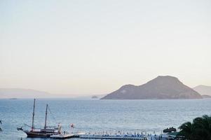 vista aérea del muelle de madera con puerto, barco turístico pirata y puerto deportivo en el complejo turco cerca de bodrum a la luz del atardecer. foto