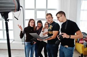 Photographer explaining about the shot to his team in the studio and looking on laptop. Talking to his assistants holding a camera during a photo shoot. Teamwork and brainstorm.