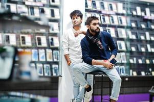 Two indians mans customer buyer at mobile phone store with earphones and wireless speaker listening music. South asian peoples and technologies concept. Cellphone shop. photo