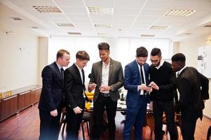 Six multiracial business mans standing at office and use mobile phones. Diverse group of male employees in formal wear with cellphones. photo