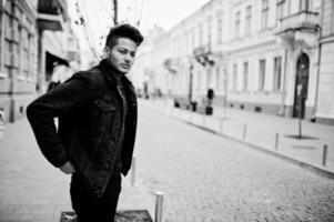 Handsome and fashionable indian man in black jeans jacket posed outdoor. photo