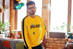 Asian man in eyewear and yellow sweatshirt posing indoor cafe with traffic light. photo