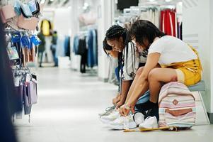 Three african woman choosing clothes at store. Shopping day. They buying shoes,sitting at bench and wear sneakers. photo