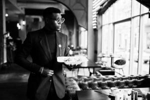 Fashionable african american man in suit and glasses standing at cafe with plate of salad in hand. photo