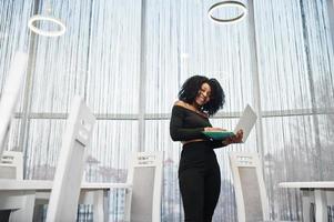 Fashionable young beautiful african american business woman with afro hairstyle wear in elegant black, stand with laptop at hands. photo