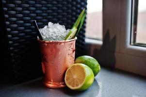 cóctel alcohólico con hielo y limón en lata de bronce en la mesa del bar. foto