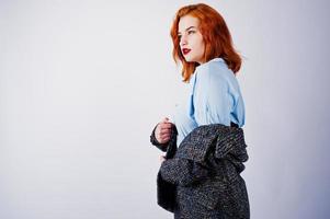 Portrait of a fantastic redheaded girl in blue shirt, grey overcoat posing with sunglasses in the studio. photo