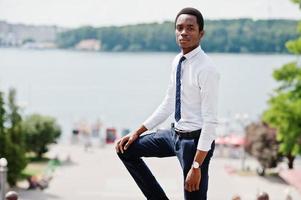 elegante hombre de negocios afroamericano con pantalones y camisa posados al aire libre contra el lago. foto