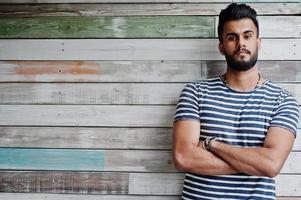 Handsome tall arabian beard man model at stripped shirt posed outdoor against wooden background. Fashionable arab guy.