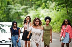 Group of five happy african american girls posed against car, one of them show keys. photo