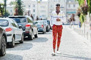 Portrait of handsome stylish african american model man in red throusers and white shirt posed at street. photo