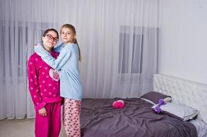 Two friends girls in pajamas having fun on bed at room. photo