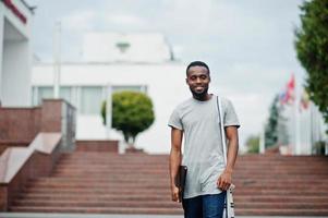 African student male posed with backpack and school items on yard of university, against flags of different countries. photo