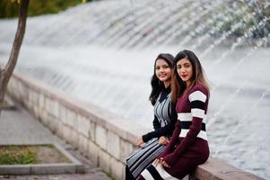 Portrait of two young beautiful indian or south asian teenage girls in dress posed against fountains. photo