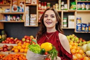 Girl in red holding different vegetables on fruits store. photo