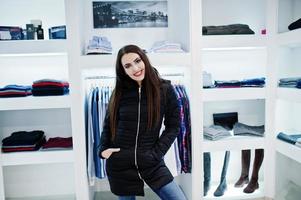 hermosa chica morena en la boutique de la tienda de ropa en la chaqueta de invierno. foto