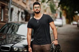 Awesome beautiful tall ararbian beard macho man in glasses and black t-shirt walking against business car. photo