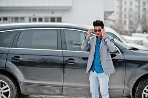 Casual young indian man in sunglasses posed against suv car. photo