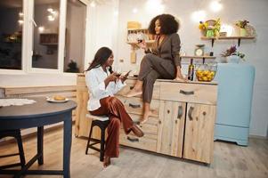 dos amigas afroamericanas que pasan tiempo en la cocina con vino. novias negras relajándose en casa. foto