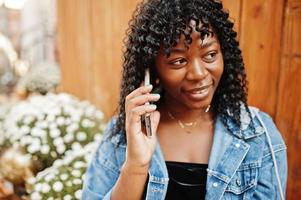 Stylish trendy afro france curly woman posed at autumn day in jeans jacket. Black african female model with mobile phone. photo