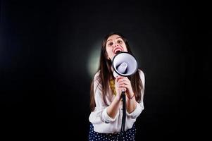 Portrait of a young woman in blue trousers and white blouse posing with megaphone in the studio. photo