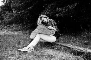 retrato de una joven y hermosa rubia positiva sentada en el suelo con un mapa en las manos en el bosque. foto