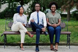 Group of three african american people posed at street of city sitting on the bench. photo