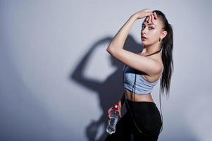 Wet cheerful attractive young fitness woman in top and black leggings with jump rope and bottle of water isolated over white background. photo