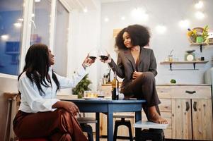 dos amigas afroamericanas que pasan tiempo en la cocina con vino. novias negras relajándose en casa. foto