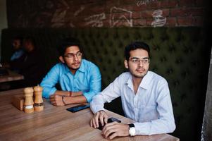 grupo de cuatro hombres del sur de asia posaron en una reunión de negocios en un café. los indios trabajan juntos con computadoras portátiles usando varios dispositivos, conversando. foto