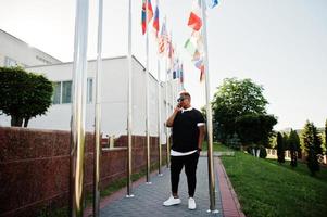 Stylish arabian muslim boy with originally hair posed on streets, against flags of different countries. photo