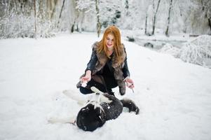 Red haired girl walking at park with husky dog on winter day. photo