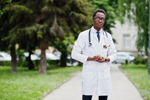 elegante médico afroamericano con estetoscopio y bata de laboratorio, con anteojos posados al aire libre. foto