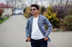 un joven indio elegante con gafas de sol usa una pose informal al aire libre. foto