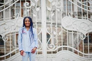 Stylish african american girl with dreads holding mobile phone at hand, outdoor against white royal gates at snowy weather. photo