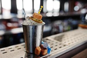 Alcoholic cocktail with sweets and candies in small silver bucket at bar table. photo