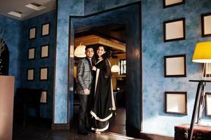 Lovely indian couple in love, wear at saree and elegant suit, posed on restaurant against wall with frames. photo