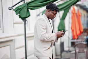 Stylish afro man in beige old school suit with mobile phone. Fashionable young African male in casual jacket on bare torso. photo