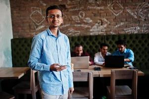 Group of four south asian men's posed at business meeting in cafe. Indians work with laptops together using various gadgets, having conversation. Indian man with mobile phone. photo