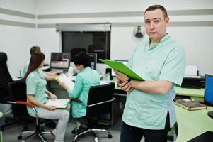 Medical theme .Portrait of male doctor with clipboard against group of doctors meeting in the mri office at diagnostic center in hospital. photo